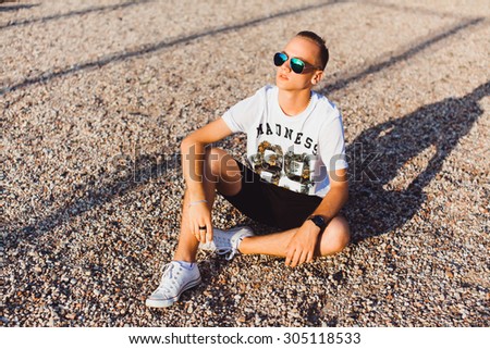 Lifestyle,Portrait of young hipster man sitting outdoors with very handsome face in white casual shirt on natural background,city street.Aviator mans sunglasses,b-boy,swagger man,stylish man