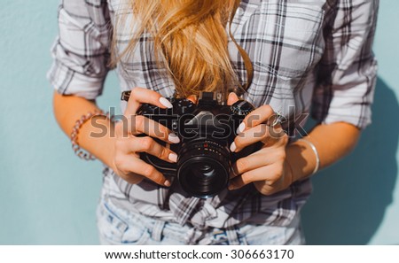 Outdoor fashion details, sexy woman wearing elegant beige clothes and holding vintage retro camera on her hands,stylish classic accessorizes,toned colors.Photographer.polaroid