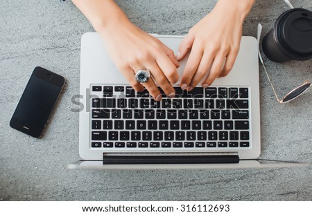 outdoor image of student, teen girls hand working on laptop at street cafe.Overhead of essentials for modern young person. on grey background.Pastel tender colors.Laptop,black phone,coffee break