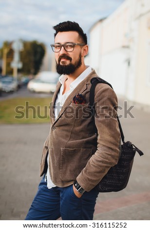 Outdoor street portrait of young fashion handsome hipster man with vintage glasses and camera,relaxing after work,weather jacket and mens accessorizes ,Hipster bearded man