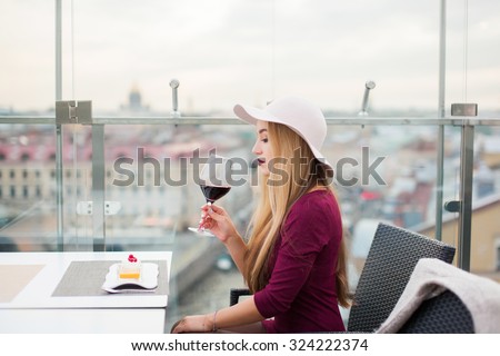 Sensual young lady drinking red wine posing at cafe with a great view of the city,lounge bar,skyline,red lipstick smile,red wine ,fancy woman,lovely fashionable style,teen fashion,fashion accessory