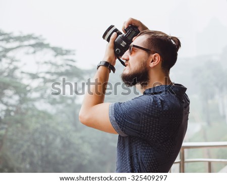 Close-up lifestyle image of handsome man photographer,making  pictures on professional camera,travel man,hiker person,man sunglasses,outdoor mans hand watch,bearded brutal man,toned,long hairstyle