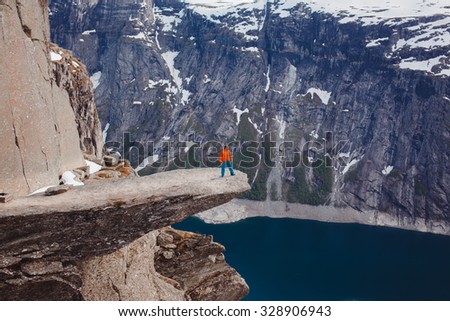 Amazing view of hiker man posing at troll tongue,at Norway mountains,freedom concept.Winter concept image of traveling man,happy,wild and free,lake.fjord.snow landscape,warm clothes,travel