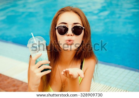 Fashion lifestyle portrait of young happy pretty woman laughing and having fun at pool party and drinking cocktail,listening favorite music at earphones,stylish vintage outfit,bright fresh colors