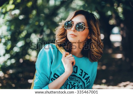 Close-up lifestyle fashion portrait of young hipster woman walking at park , travel with backpack, stylish casual outfit, evening sunset, reflecting sunglasses student, bright make up bf hairstyle
