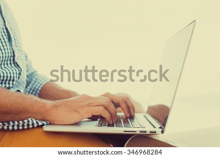 stylish young man in a shirt and shorts and sneakers working on laptop while sitting on the beach on the pier, sending mail, mounts, video editing and photography
