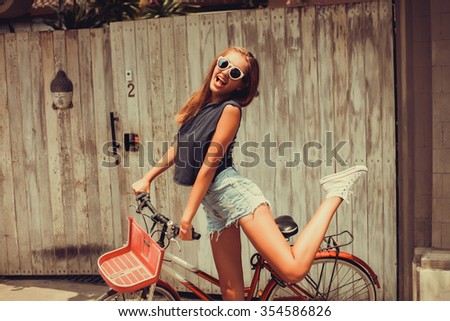 young beautiful girl in a blue t-shirt denim shorts, sunglasses and sneakers posing with red retro bike crazy girl happy joyful mood cheerful smiles on the lips red lipstick