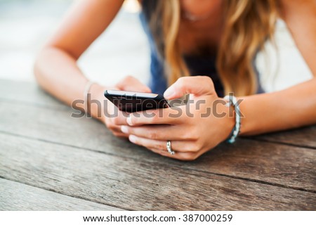 young cute girl hipster, sitting at a cafe holding a smart phone, answering texts, phone calls, letters, posts photos in instagram, outdoor portrait, close up, elaborated and bracelets on the hands
