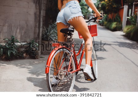 beautiful girl in denim shorts, sneakers, posing sitting on a vintage red bike, beautiful sport sexy ass, long street, outdoor portrait, close up, bicycle