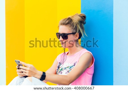 young blonde girl in sunglasses posing sitting on the floor near a colored wall, my phone and smart watch, girl in sneakers and jeans,works, photos,social networks,facebook, instagram,outdoor portrait