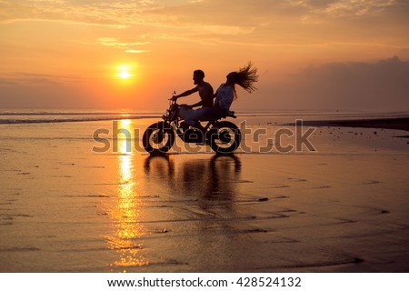 young beautiful couple hipsters in stylish clothing for a retro motorcycle on the street, outdoor portrait,posing in jeans and t-shirts,bearded guy,blonde girl,travel together go on the water splashes