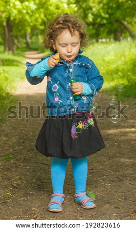 little curly girl with soap bubbles in the park