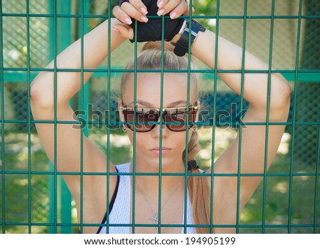 beautiful athletic girl in sunglasses looking through the bars at the park