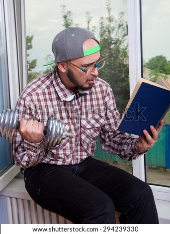 Funny nerd reading a book and picks up a dumbbell in the interior