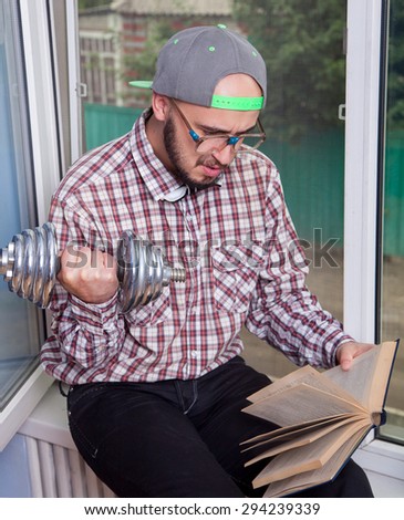 Funny nerd reading a book and picks up a dumbbell in the interior