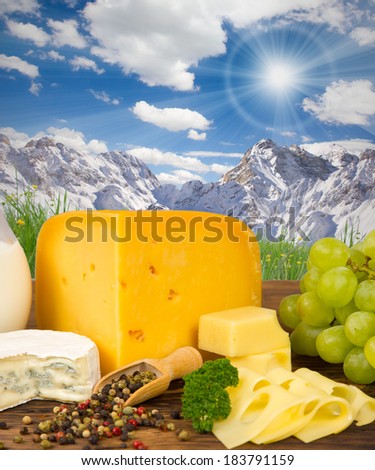 Photo of cheese and fruit on wooden board with mountains