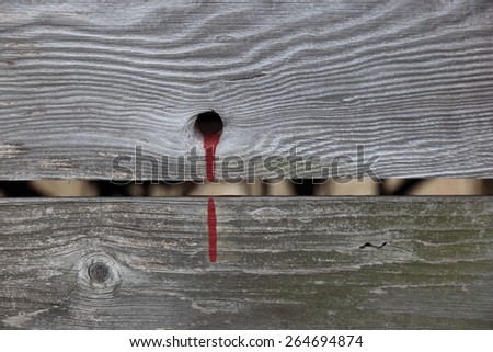 Weathered barn planks with textured gray surface, knots, blood like red paint spilled from a hole, interrupted by a gap.