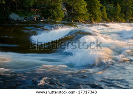 Fast streaming river in the woods at sunset. Water is in motion blur.