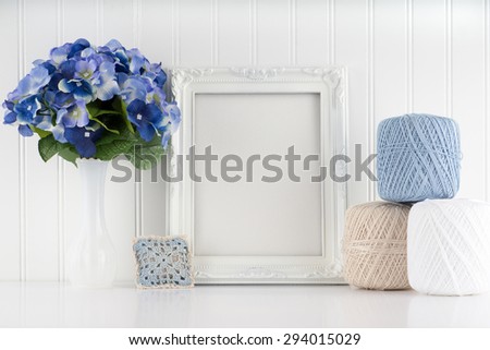 Blue and white hydrangea on a white table in front of a white bead-board wall with small crocheted pillow, and stack of crochet thread spools