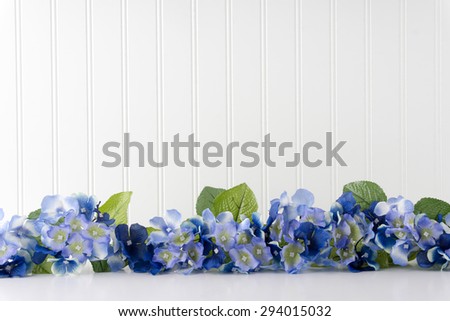 Blue and white hydrangea on a white table in front of a white bead-board wall