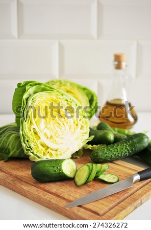 Sliced fresh cucumbers and cabbage, olive olive\'s jug on the kitchen desk.