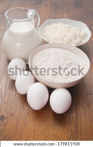 Jug with milk, flour and eggs on a wooden table