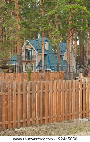 Modern country house in the pine forest behind a wooden fence