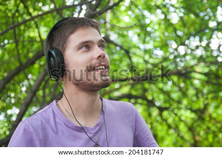 Young man listens to music on headphones in a summer park