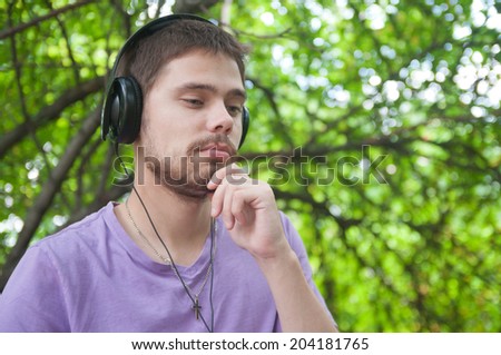 Young man listens to music on headphones in a summer park