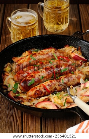 Sausages fried in cast iron skillet with two beer mugs on wooden background