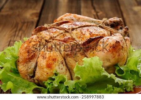 Bondage shibari roasted chicken with salad leaves on red plate on wooden background  closeup horizontal