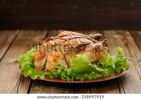 Bondage shibari roasted chicken with salad leaves on red plate on wooden background with dark space horizontal