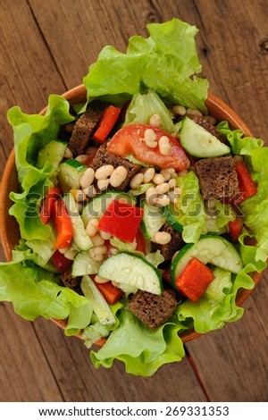 Vegetable salad with white beans, rye toasts, tomatoes, cucumber and lettuce in round bowl on wooden background topview
