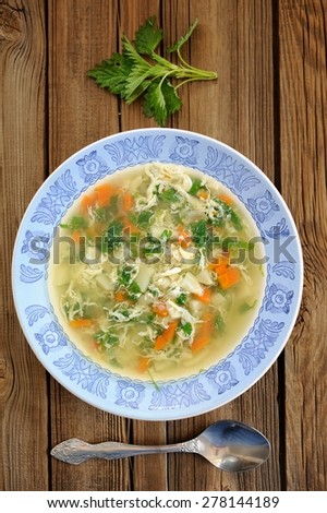 Nettle soup with eggs in blue plate with fresh nettle and spoon on wooden background vertical