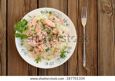 Salmon with rice, scallion and cilantro in white plate with fork on wooden background copyspace top view
