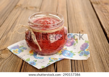 Homemade strawberry jam in open glass jar with hempstring on paper napkin