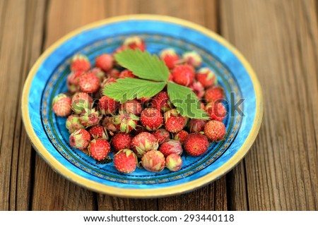 Wild strawberries Fragaria viridis in blue plate with green strawberry leaf selective focus