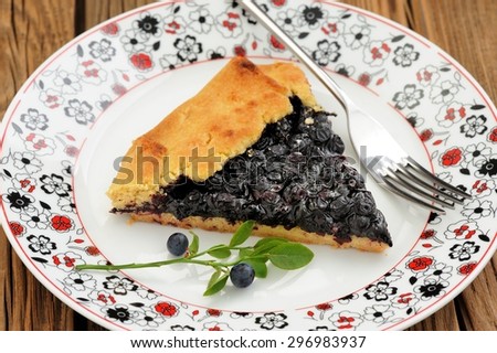 Piece of homemade vegan galette with wild blueberry on painted plate with fork decorated with green blueberry twig