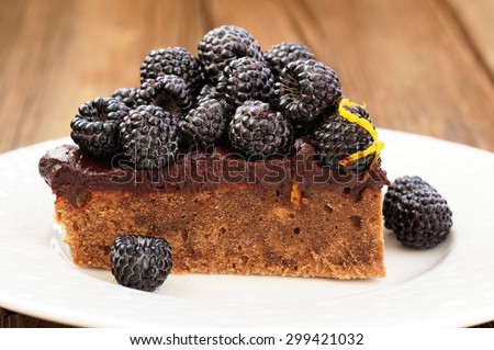 Piece of homemade yummy chocolate pie with ganache, fresh blackberries and lemon peel decorated with icing sugar in white plate on wooden table