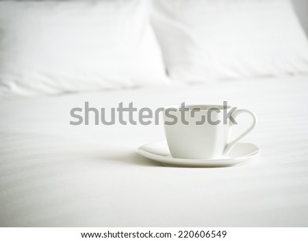Coffee cup on bed and white bed linen with Blurred pillows background