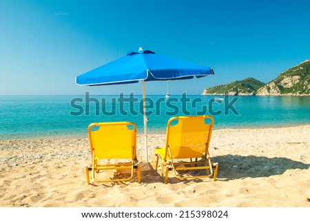 Yellow sunbeds and blue umbrella on a beautiful beach in Corfu Island, Greece Parasols and sunbeds into the sun on a tropical beach.
