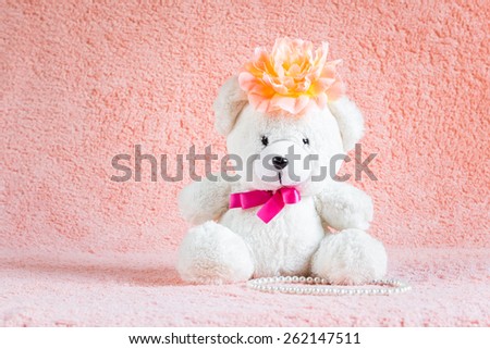 White teddy bear toy with orange flower barrette on head sitting on pink terry background
