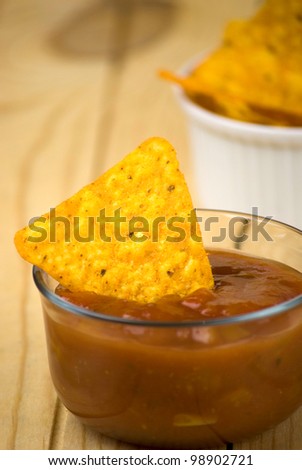 spicy tortilla chips and tomato salsa dip over wooden board