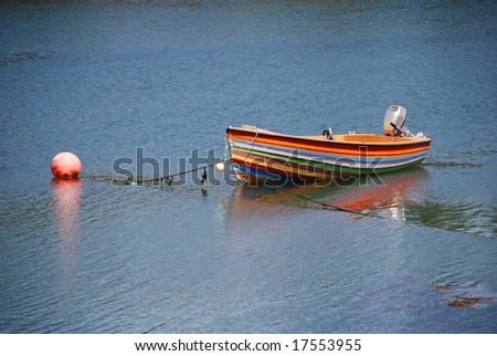 a pretty little rainbow colored ship with outboard motor floats in the water