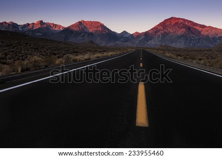 The Mountains are calling.  A highway leading to the mountains at dawn.  The morning light casts alpenglow on the peaks.