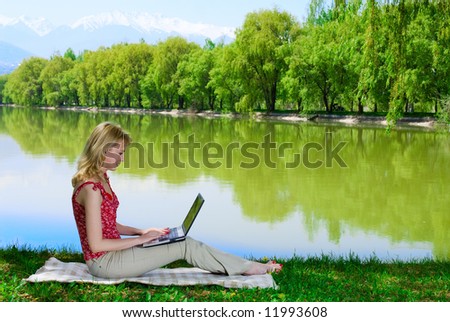 Beautiful young woman with laptop near the lake surfing the Net