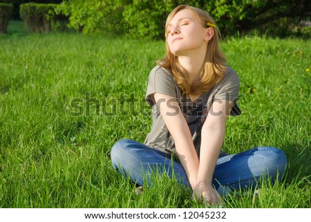 Peaceful pretty young woman sitting on the grass, enjoying the sun, life and nature