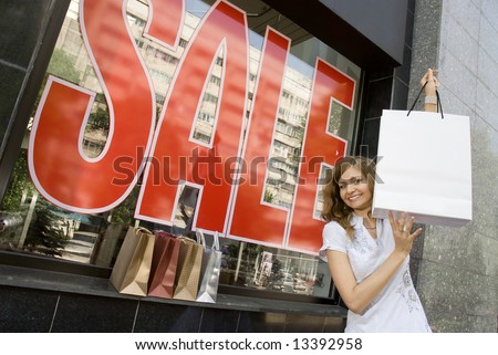 Woman holding blank white shopping bag in her arms near shop window with sale sign