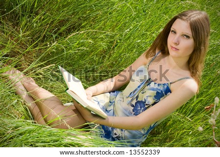 Cute young romantic girl reading an interesting book, sitting in tall grass