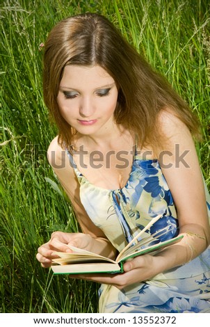 Cute young romantic girl reading an interesting book, sitting in tall grass